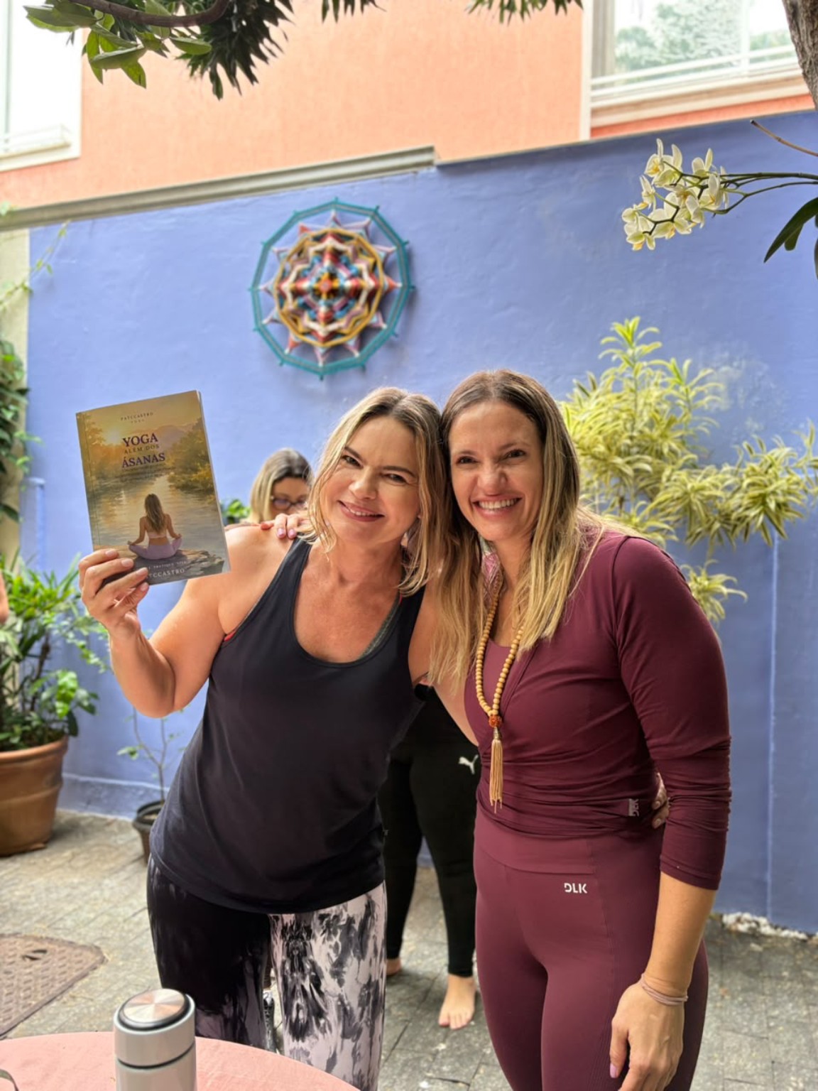 Duas participantes juntas diante da parede azul da Casa 111