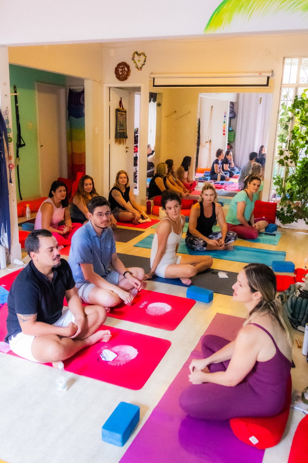 Vista da sala com instrutora e participantes sentadas em seus tapetes